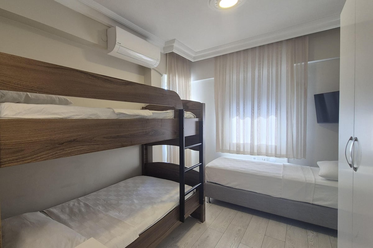 A bunk bed room with a wooden headboard, a single bed, a flat-screen TV, and an air conditioning unit.