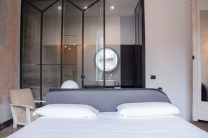 A modern bedroom with a large bed, a chair, and a bathroom visible through a glass partition. - Tutt 'e Sant Luxury Rooms (Naples)