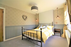 A bedroom with a bed, a wall-mounted heart decoration, and a small wooden shelf. - Hurst Cottage (Hassocks)
