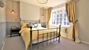 Une chambre à coucher avec un lit, une table de chevet, une lampe, une fenêtre et des rideaux.