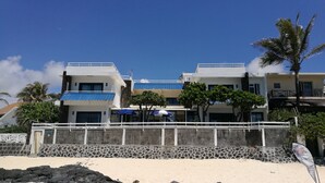A beachfront hotel with a white facade, blue accents, and a stone wall in the foreground. - Blue Beryl Guest House (Blue Bay)