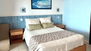 A bedroom with a bed, two bedside tables, a nightstand, a wall-mounted picture, and a blue accent wall. - Blue Beryl Guest House (Blue Bay)