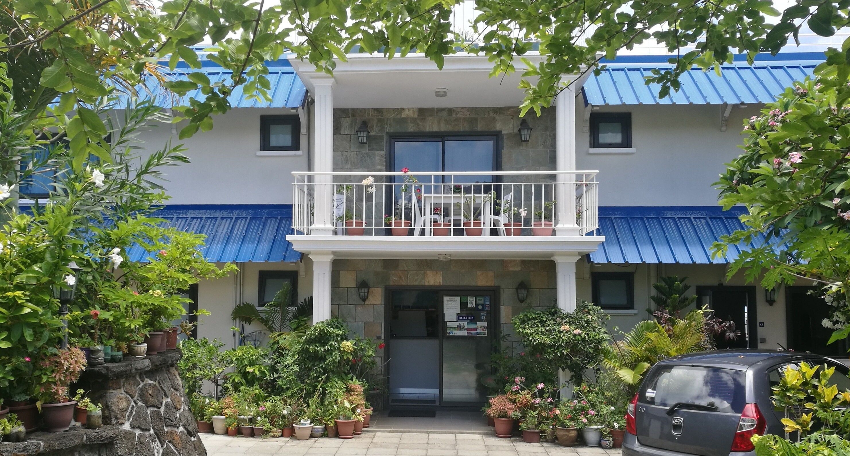 A two-story building with a balcony, stone steps, and potted plants.