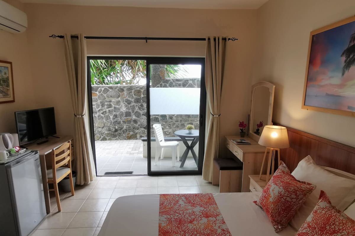 A hotel room with a bed, a desk, a television, and a view of the outdoor area through a sliding glass door.