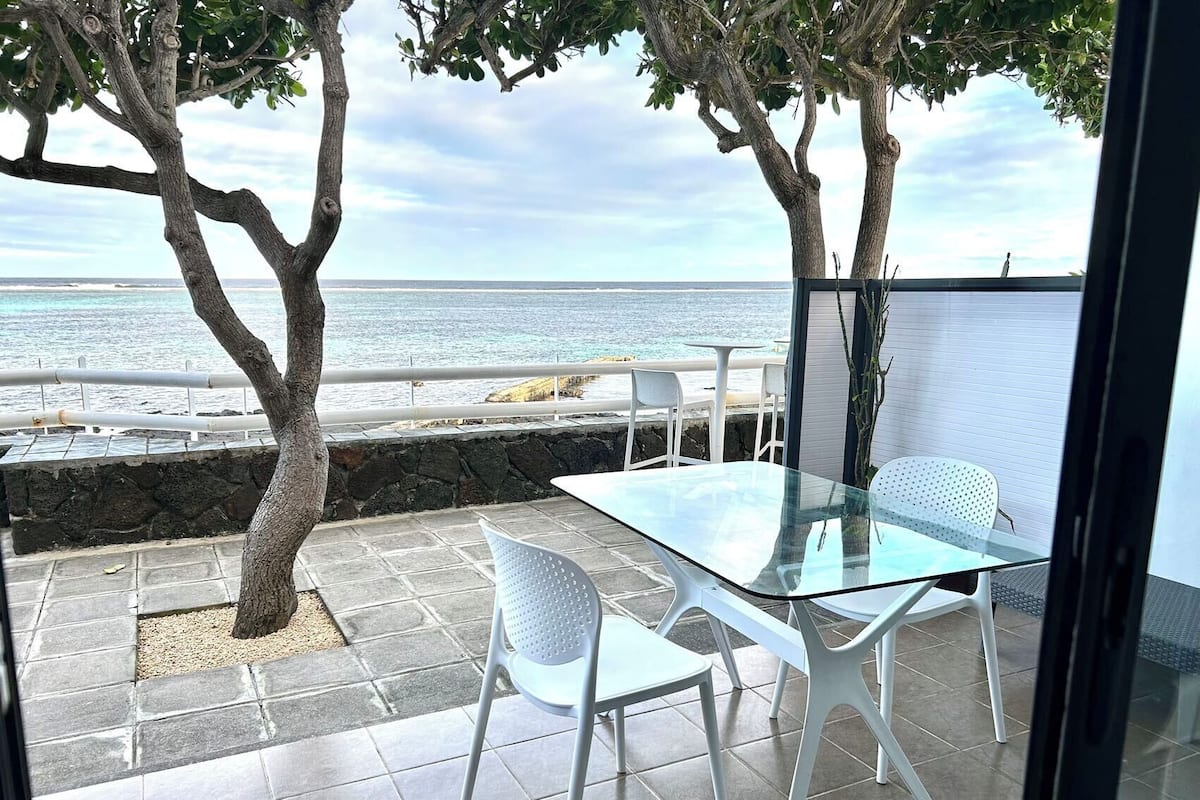 A glass table and chairs on a patio with a view of the ocean.
