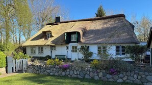 Une maison blanche avec un toit de chaume, un mur de pierre et un banc dans le jardin.
