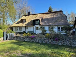 A white house with a thatched roof, a stone wall, and a bench in the front yard.