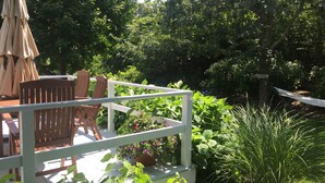 A wooden deck with a white railing, surrounded by lush greenery and a hammock.
