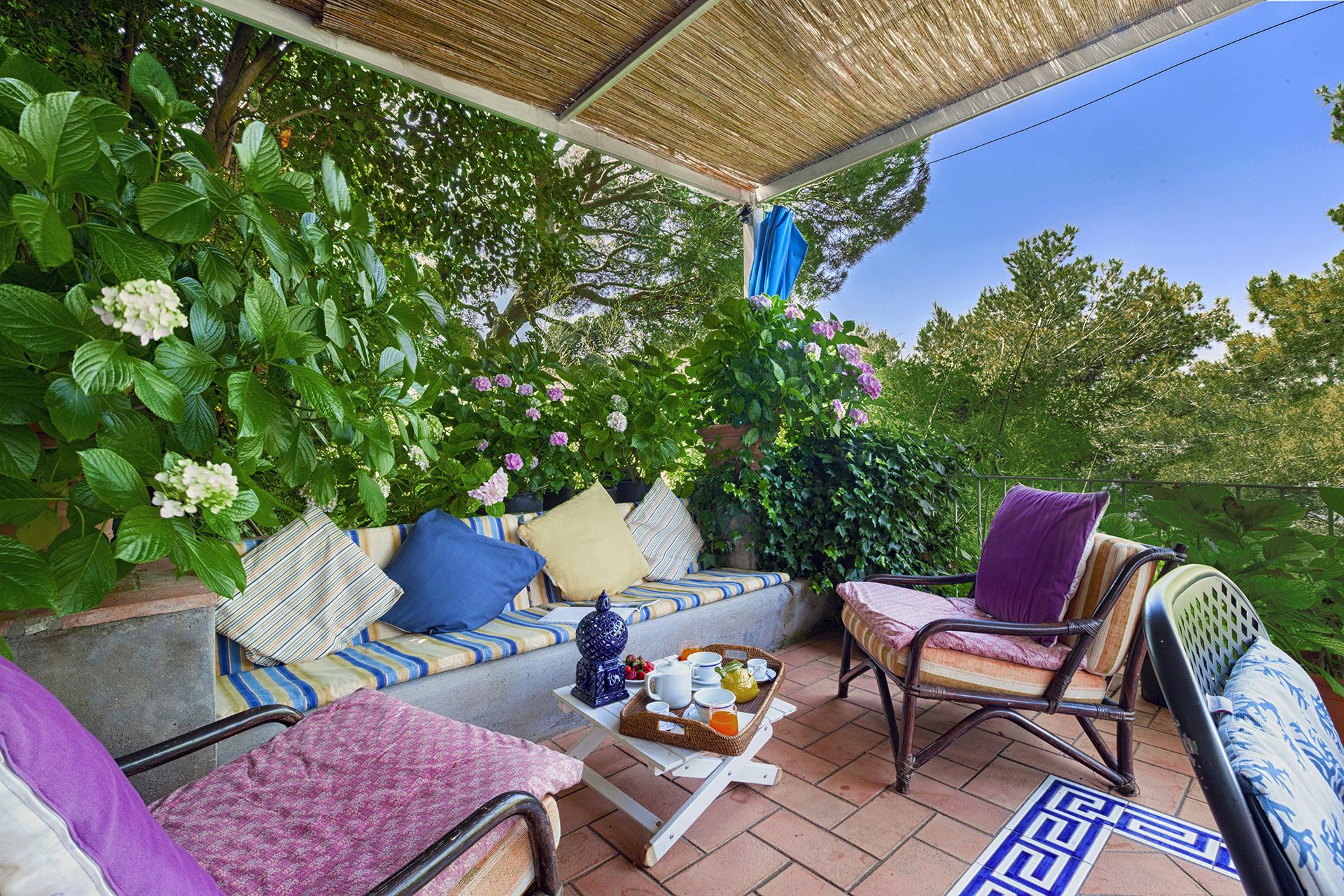 A covered patio with a sofa, chairs, and a table with breakfast items.