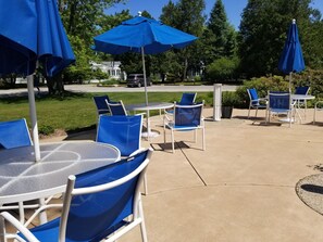An outdoor patio area with tables and chairs, blue umbrellas, and a paved walkway.