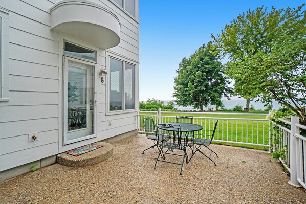 A covered patio with a table and chairs, a white fence, and a tree.