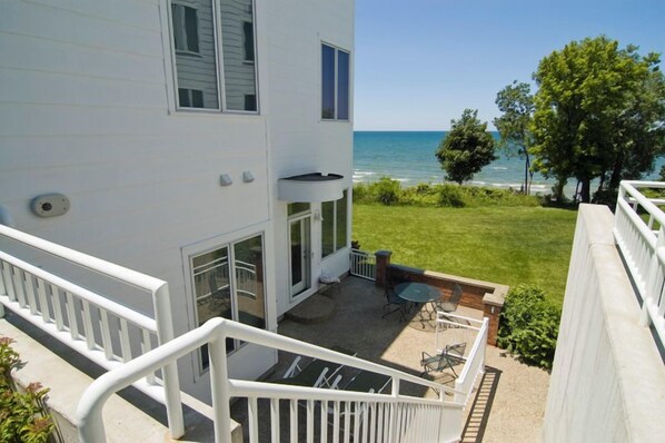 A two-story building with a balcony, a patio area with outdoor furniture, and a view of the ocean.