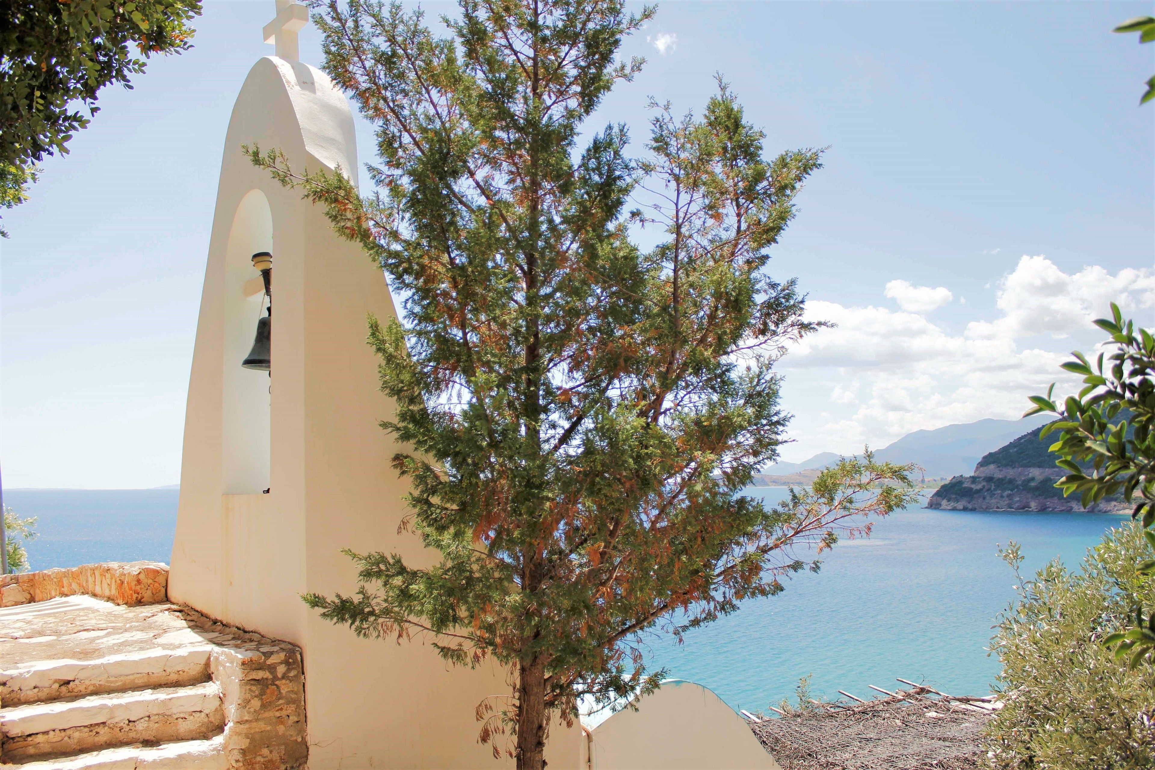 A coastal view with a white bell tower, steps leading down, and a tree in the foreground.