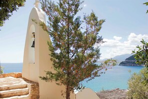 A coastal view with a white bell tower, steps leading down, and a tree in the foreground. - Muses Seaside Villas (North Kynouria)