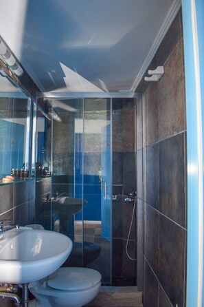 A modern bathroom with a glass shower enclosure, a sink, and a toilet. - Muses Seaside Villas (North Kynouria)