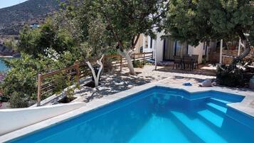 A swimming pool with a wooden deck, surrounded by trees and a view of a hillside.