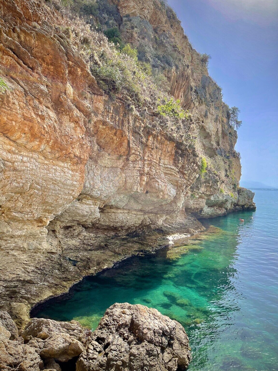 A coastal cliff with clear water and rocky formations.