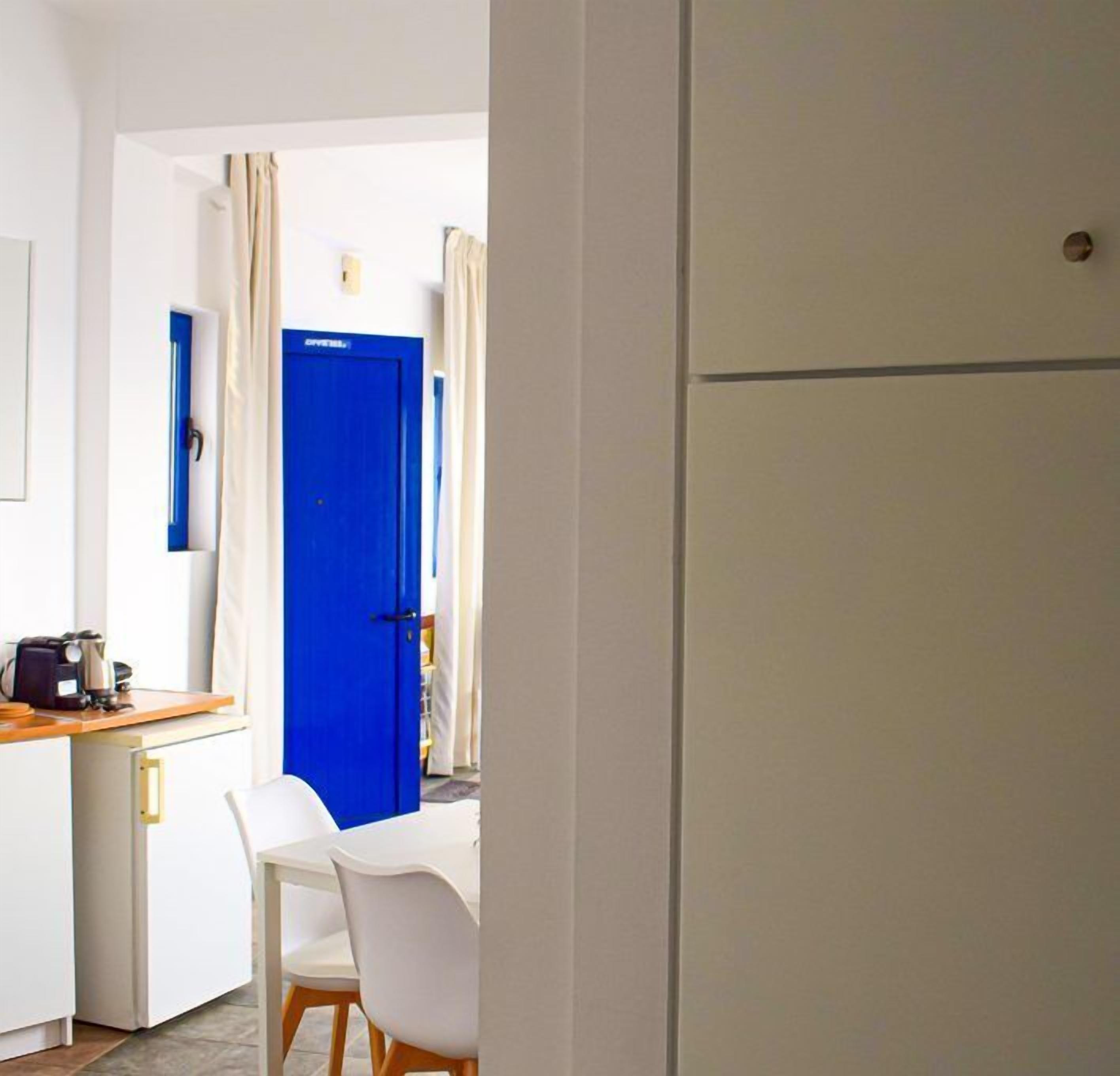 Habitación de hotel compacta con kitchenette, zona de comedor y puerta azul.
