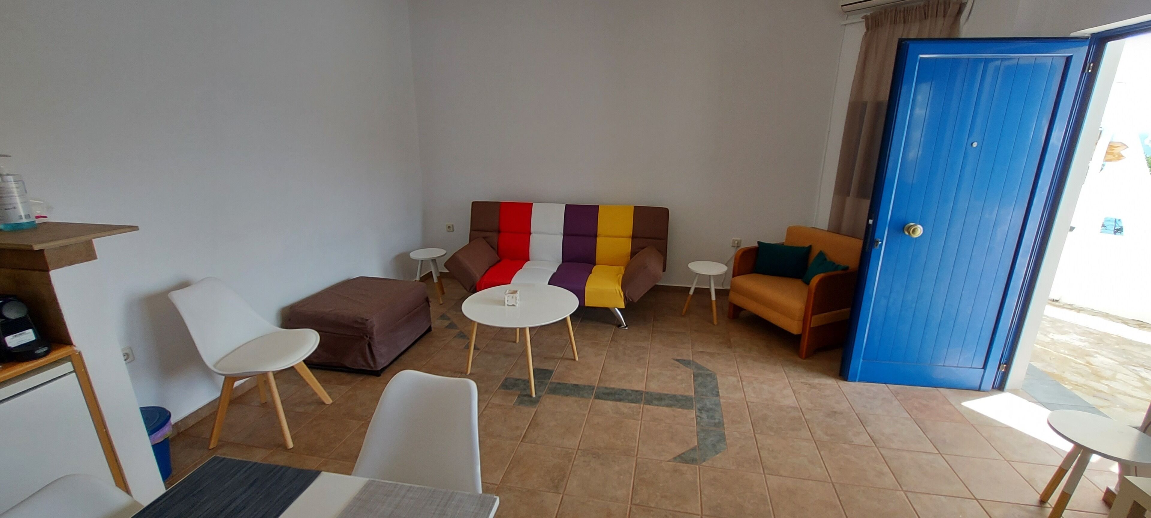 Una habitación pequeña amoblada con un sofá, dos sillas, una mesita y una puerta azul.