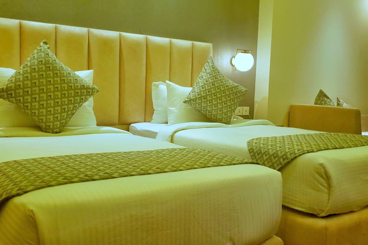 Habitación de hotel con dos camas, cada una con cabecera, almohadas y mesita de noche.