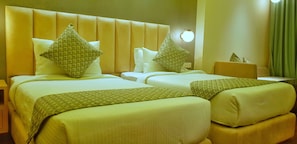 A hotel room with two beds, each with a headboard, pillows, and a bedside table.