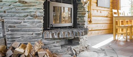 A stone fireplace with a TV, wood logs, and a dining area with wooden chairs.