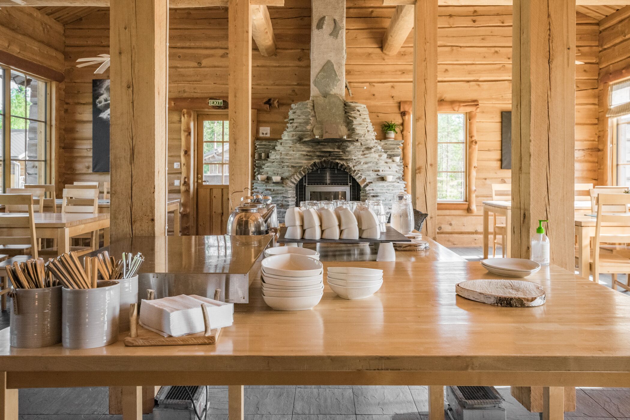 Un interior rústico de madera con chimenea de piedra, mesas de comedor y diversos utensilios de cocina.