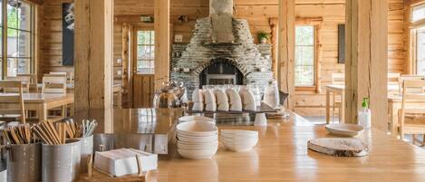 Un interior rústico de madera con chimenea de piedra, mesas de comedor y diversos utensilios de cocina.