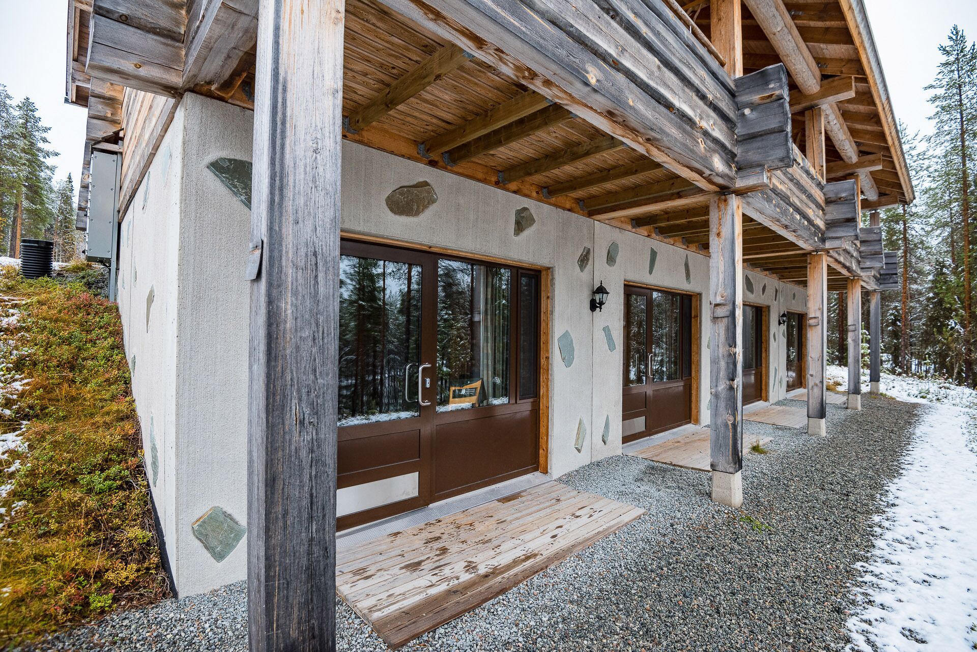Una cabaña de madera con ventanas amplias y fachada de piedra, ubicada en un bosque nevado.