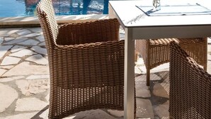A poolside area with wicker furniture, a table, and tropical plants. - Villa Thea (Pegeia)
