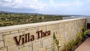 A stone wall with the name "Villa Thea" and a view of a hilly landscape in the background. - Villa Thea (Pegeia)
