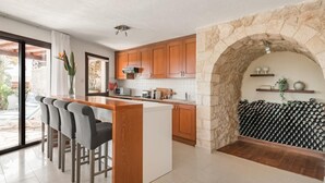 A modern kitchen with wooden cabinets, a stone archway, and a bar area with stools. - Villa Thea (Pegeia)