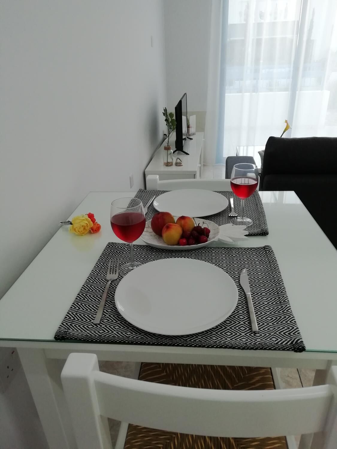 A dining table set with plates, cutlery, a glass of red wine, and a bowl of fruit.
