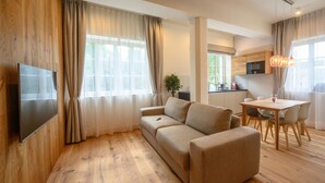 A modern living room with a sofa, a TV, a dining area with a table and chairs, and a kitchen in the background.