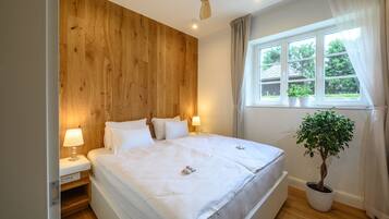 Een slaapkamer met een houten hoofdbord, een bed met witte lakens, twee nachtkastjes met lampen, een plafondventilator, een raam met gordijnen en een potplant.
