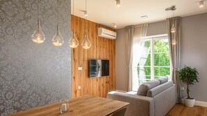 A modern living room with a wooden wall, a flat-screen TV, a sofa, a dining table, and hanging light fixtures.