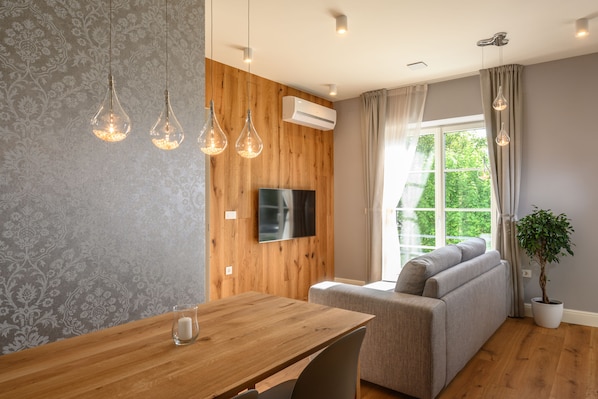 Una sala de estar moderna con una pared de madera, un televisor de pantalla plana, un sofá, una mesa de comedor y lámparas colgantes.