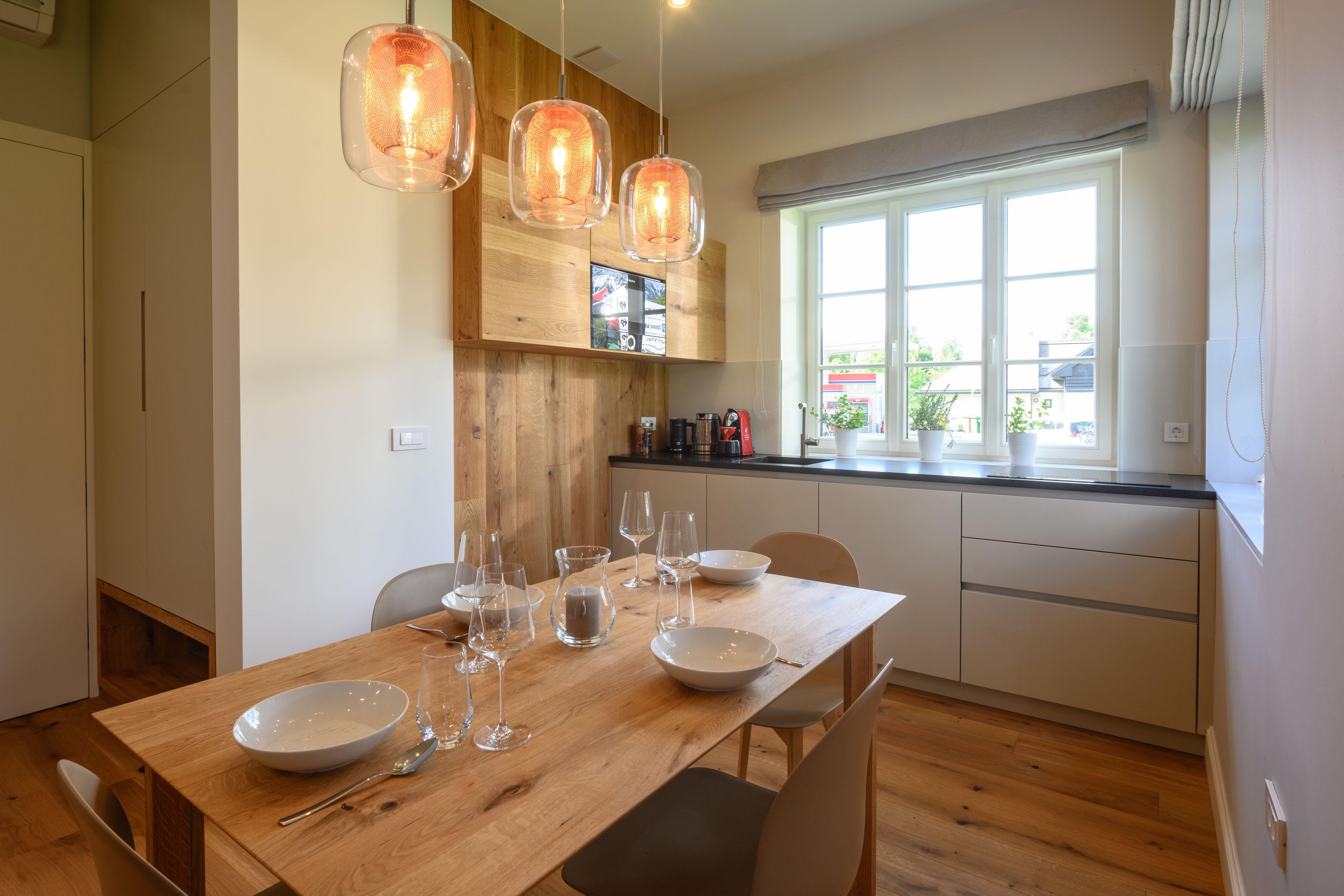 Un comedor con una mesa de madera dispuesta para cuatro personas, rodeada de sillas. Hay lámparas colgantes sobre la mesa.