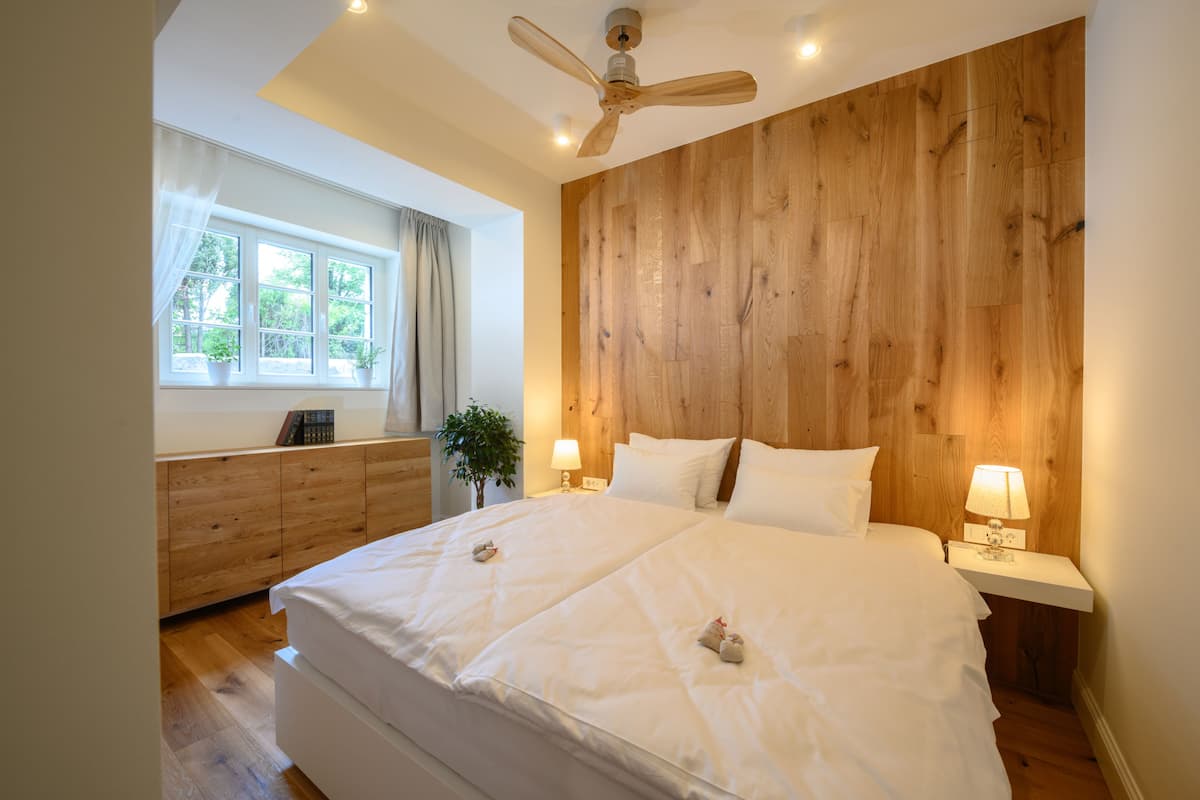 Un dormitorio con una cama grande, pared de paneles de madera, lámparas de noche y un ventilador de techo.