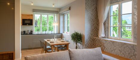 A modern kitchen with a dining area, a sofa, and a large window with curtains.