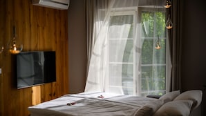 A bedroom with a bed, a TV mounted on the wall, and a window with sheer curtains.