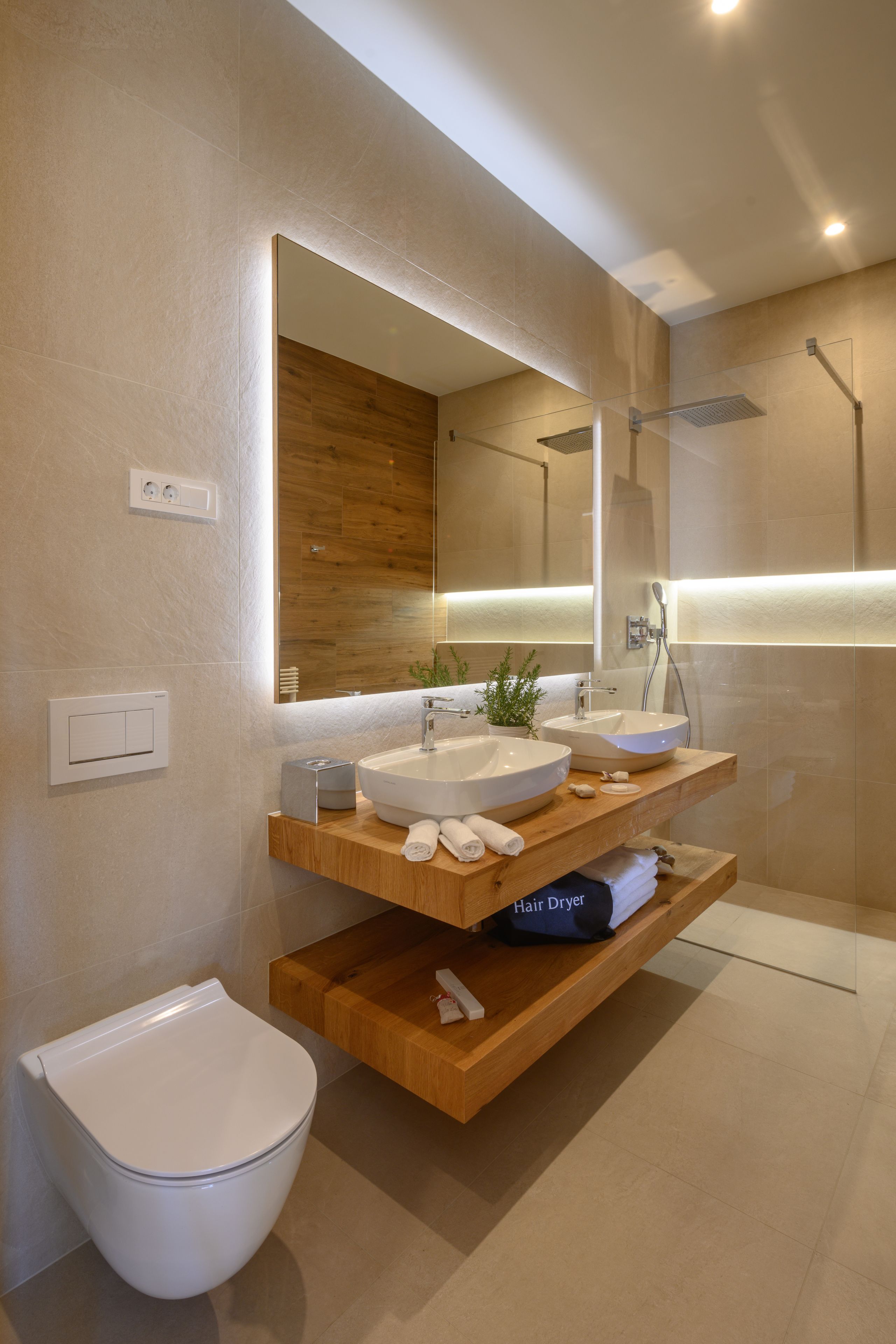 Un baño moderno con dos lavamanos, inodoro, secador de pelo y ducha.