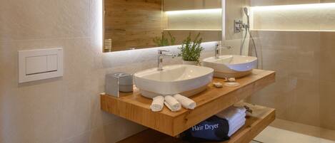 A modern bathroom with two sinks, a toilet, a hair dryer, and a shower.