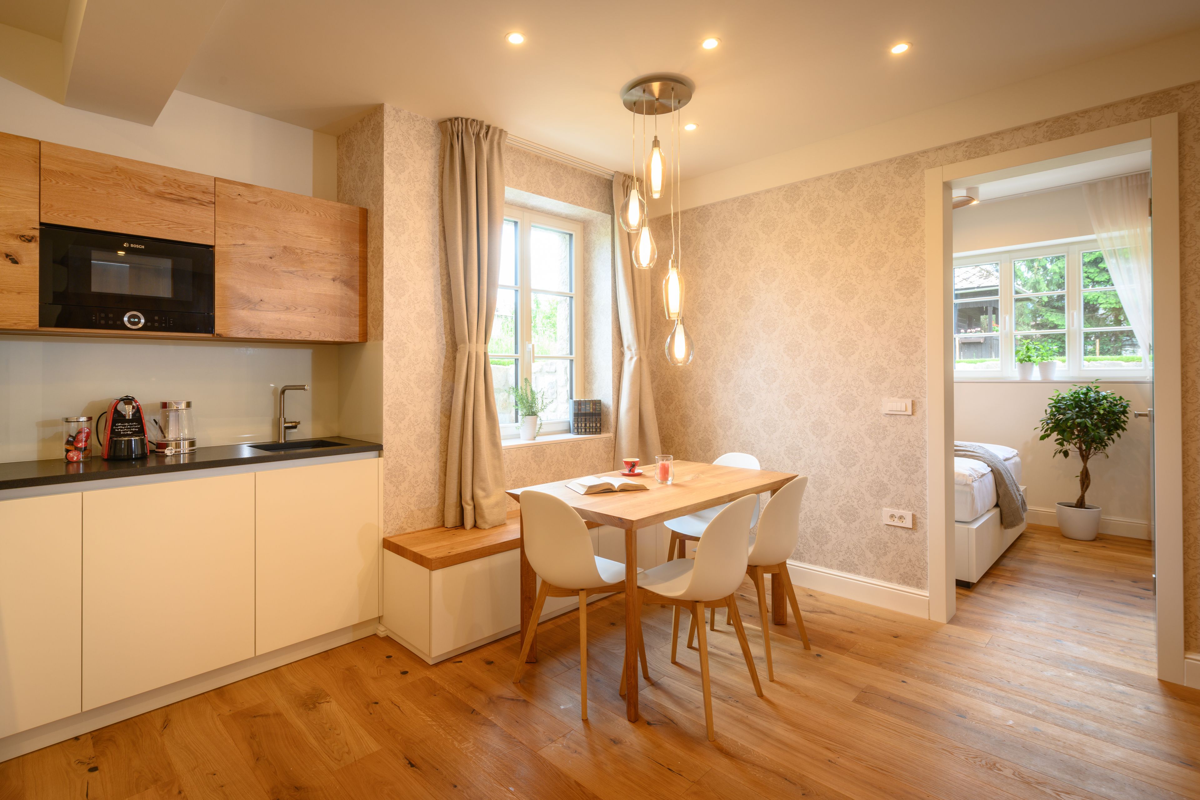 A modern kitchen with wooden cabinets, a built-in microwave, and a dining area with a table and chairs.