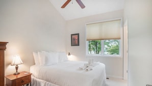 Una camera da letto con un letto, un comodino con una lampada, una finestra con persiane e una ventola a soffitto.
