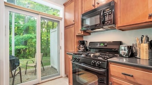 Una cucina con mobili in legno, un fornello, un forno a microonde e una porta vetrata scorrevole che dà su un patio.