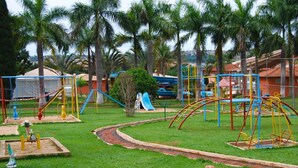 A playground with various play structures, surrounded by palm trees and a brick pathway. - Estancia Park Hotel (Anapolis)