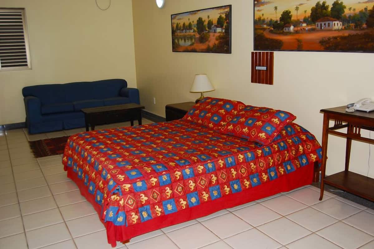 Une chambre à coucher avec un lit, un canapé bleu, une table de chevet avec une lampe et deux tableaux accrochés au mur.
