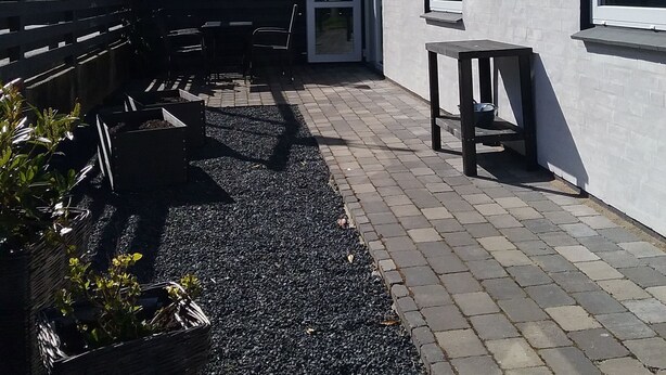 A patio area with a gravel path, outdoor furniture, and a building with a white exterior and large windows. - Hals Hotel Apartment (Hals)
