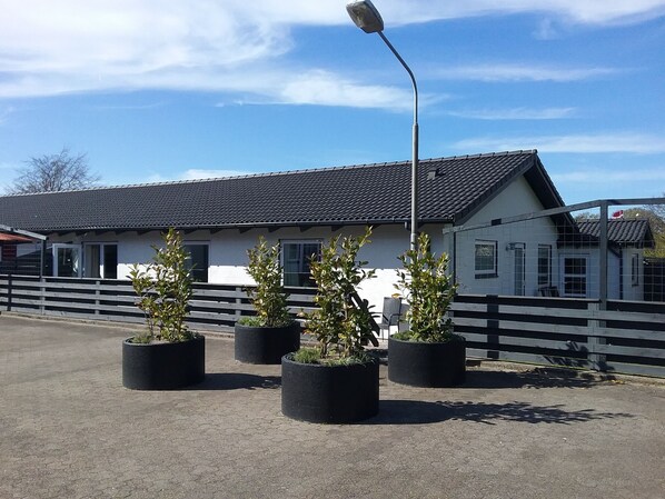 A building with a tiled roof, a fenced area with potted plants, and a street lamp. - Hals Hotel Apartment (Hals)